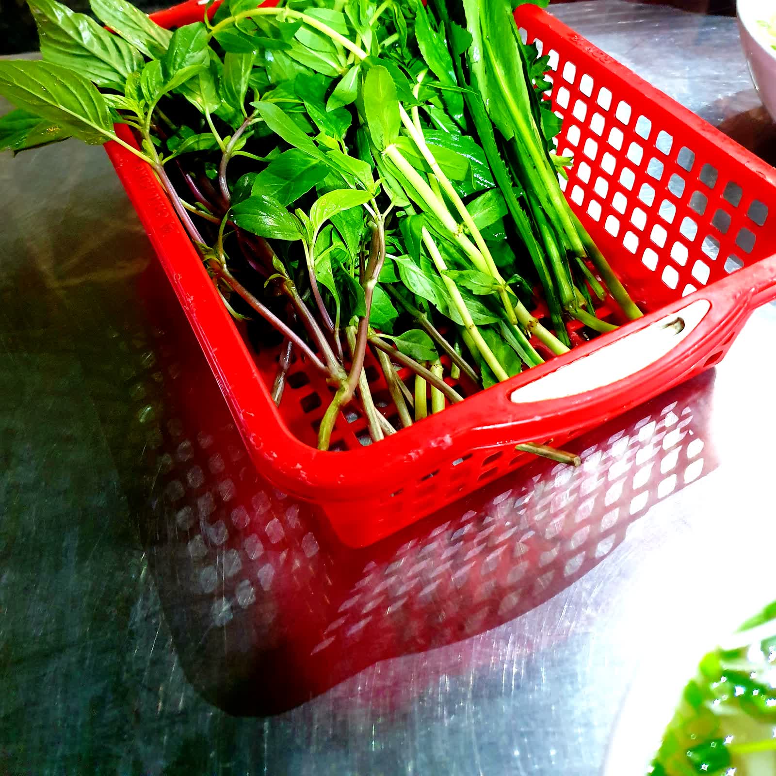 Rổ rau thơm húng quế, ngò gai ăn kèm trên bàn một quán phở khác, không phải rau của quán này